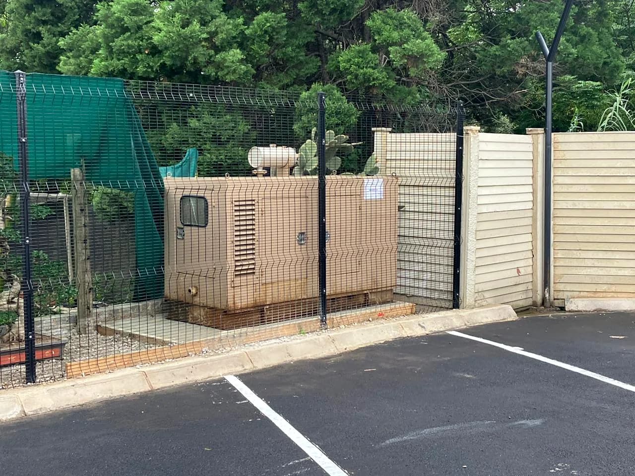 Canopied generator inside a mesh security cage beside an office car park