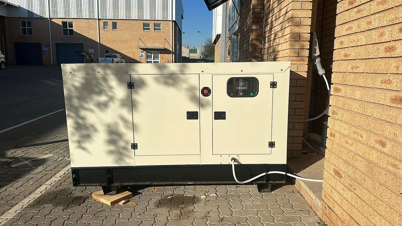White silent diesel generator against a face-brick wall at an industrial business park