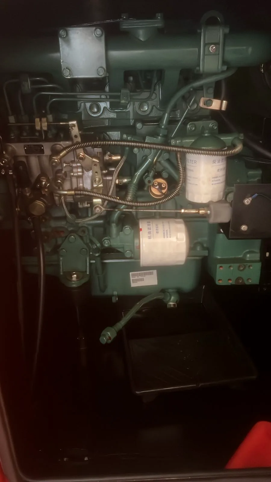 Green diesel engine inside a generator canopy, with its fuel filter, injection pump and pipework