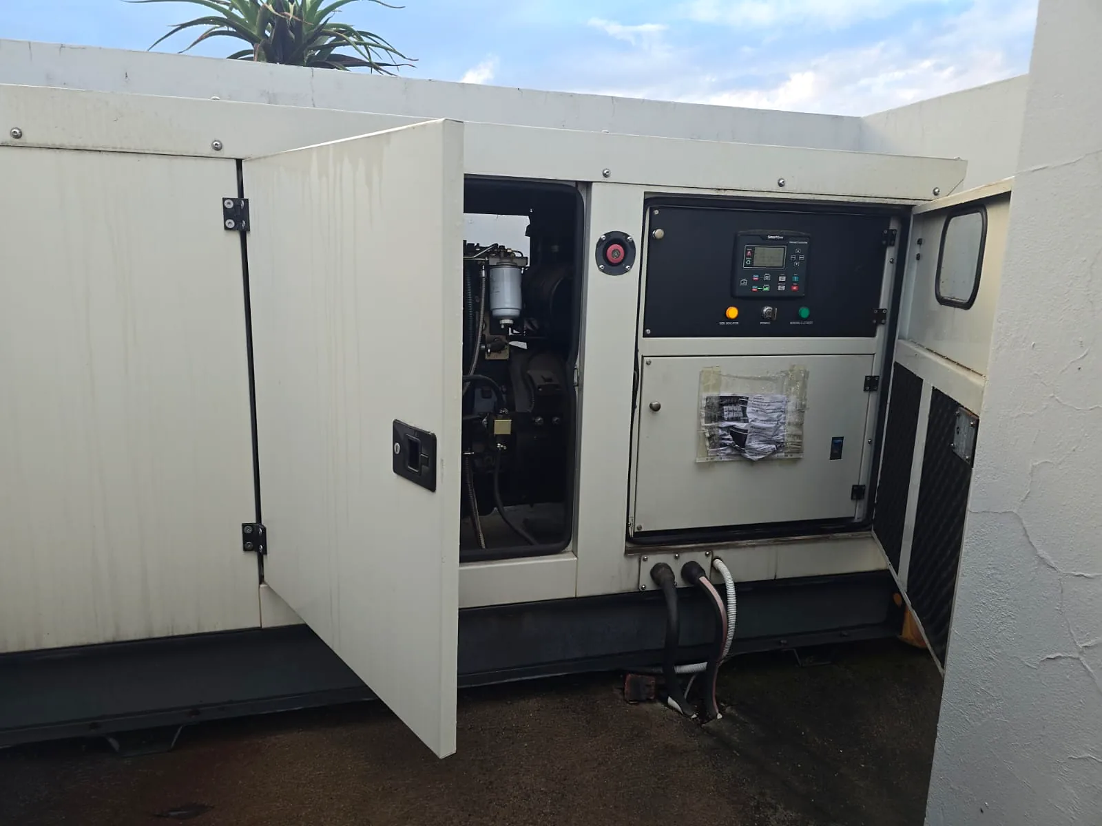 SmartGen genset controller in the control panel of an open diesel generator canopy, with the engine and cable entries visible