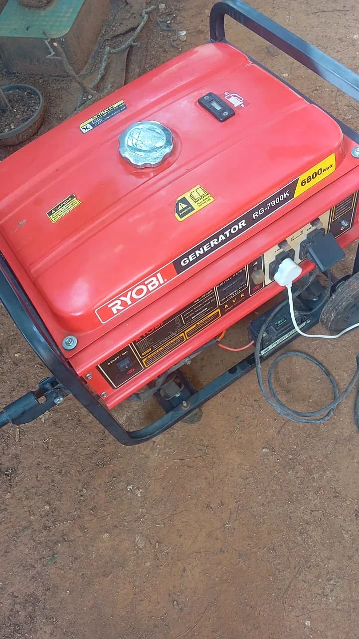 Red Ryobi petrol generator seen from above in a dirt yard, with plugs connected to its sockets