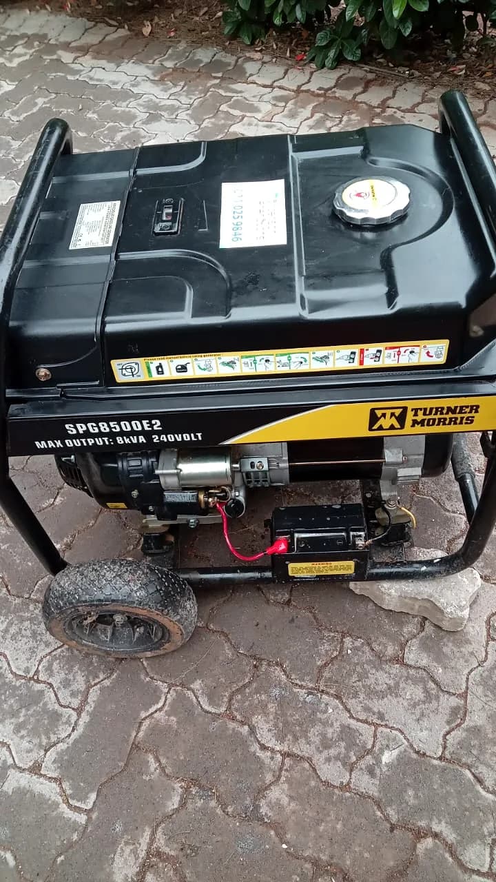 Black Turner Morris SPG8500E2 petrol generator with its starter battery, on paving