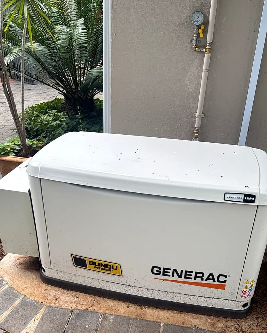 Generac home standby generator against a house wall, with the gas supply pipe and pressure gauge on the wall above it