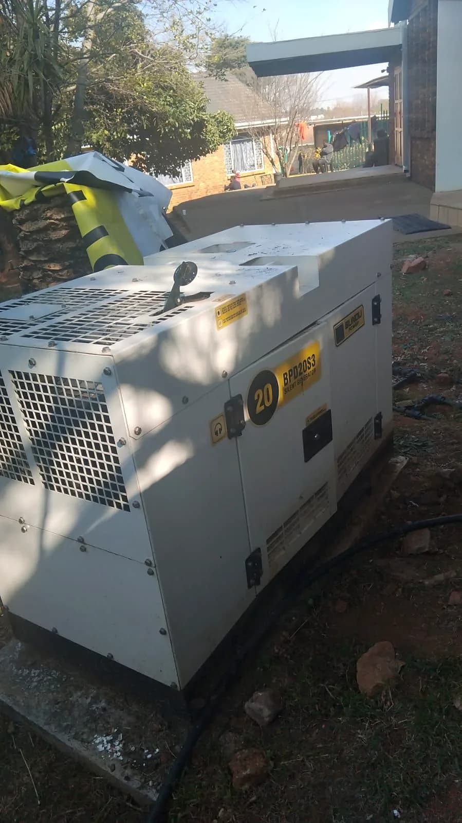 Grey silent diesel generator on a concrete slab in a garden beside a house