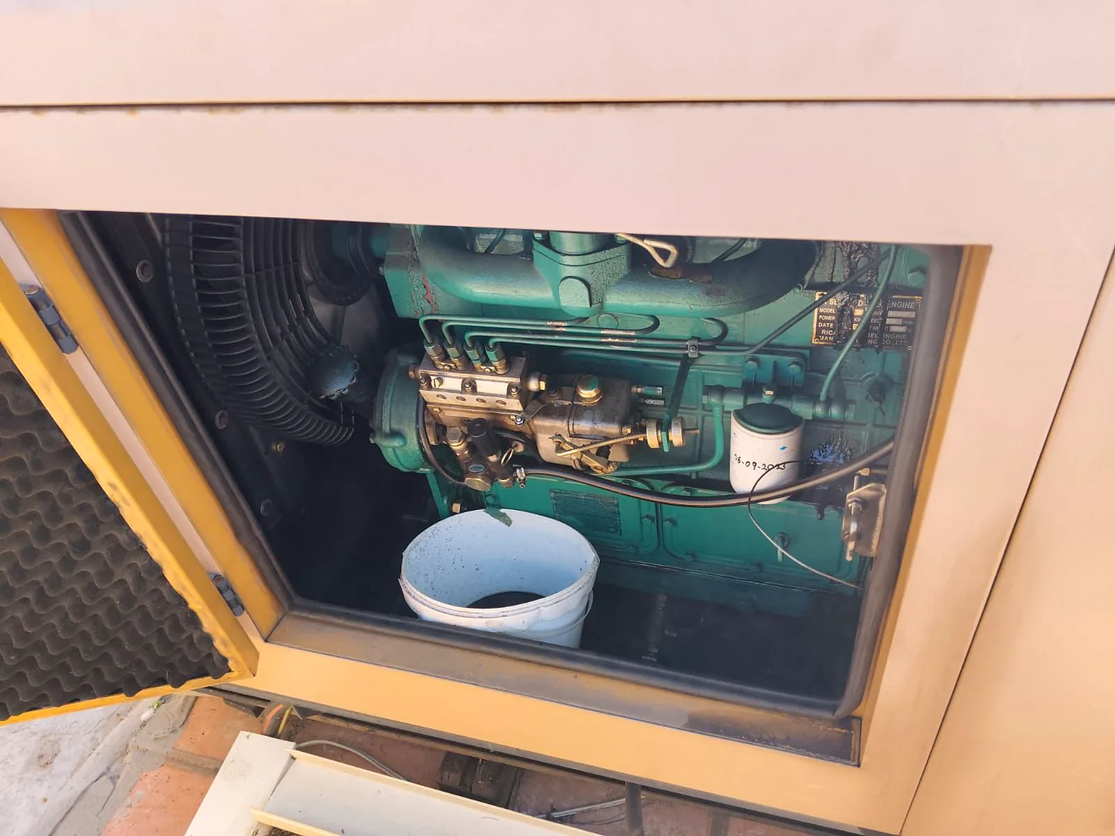 Generator canopy door open during a service, with a bucket under the diesel engine to catch the drained oil